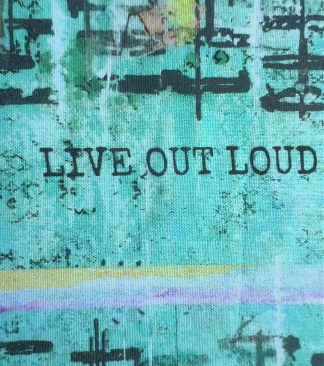 a short video demonstrating the angles of a vibrant blue green fabric reusable book cover with the words, 'live out loud' printed on the top.