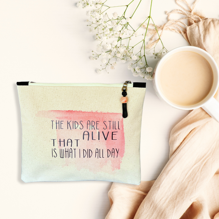a square canvas zip bag with pink watercolor swash and the words, "the kids are still alive. THAT is what I did all day." in black lettering. plus a coffee cup, a scarf and a white flower