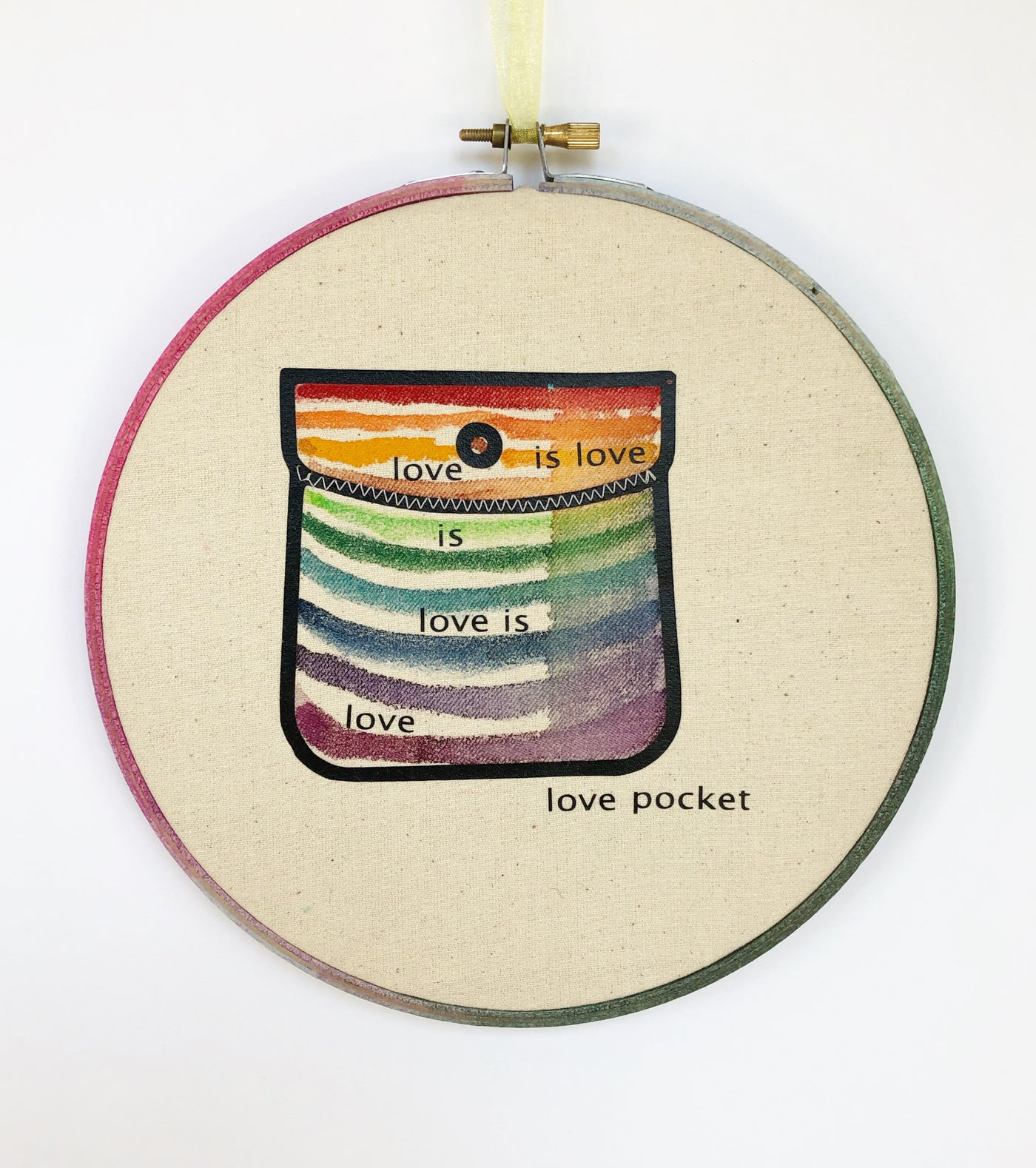 round wooden hoop with canvas and a multicolored striped painted pocket with the words, "love is love is love...love pocket."