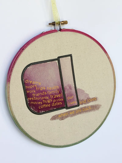 round wooden painted hoop with canvas and a painted pocket on its side, with the words "dreams, hopes, trips, health, friends, family, travel, hugs, drinks, coffee dates, our lives and loves" spilling out.