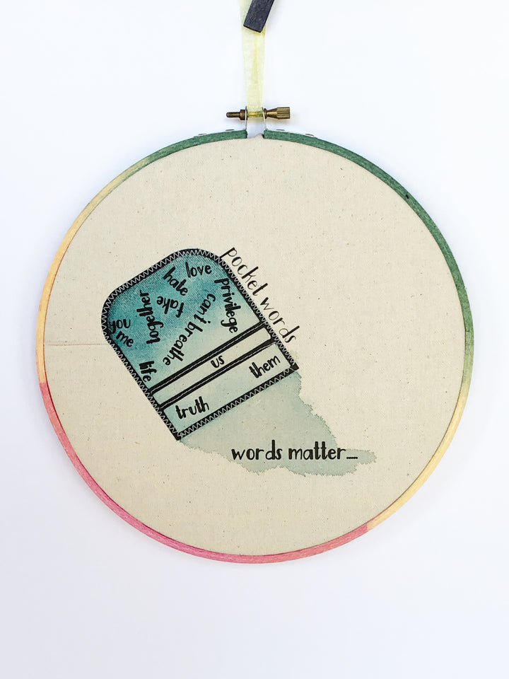 a canvas hoop art piece with a blue painted upside down pocket and the words, "you, me life together love fake, hate, privilege, can't breathe, truth, us, them and words matter.." 