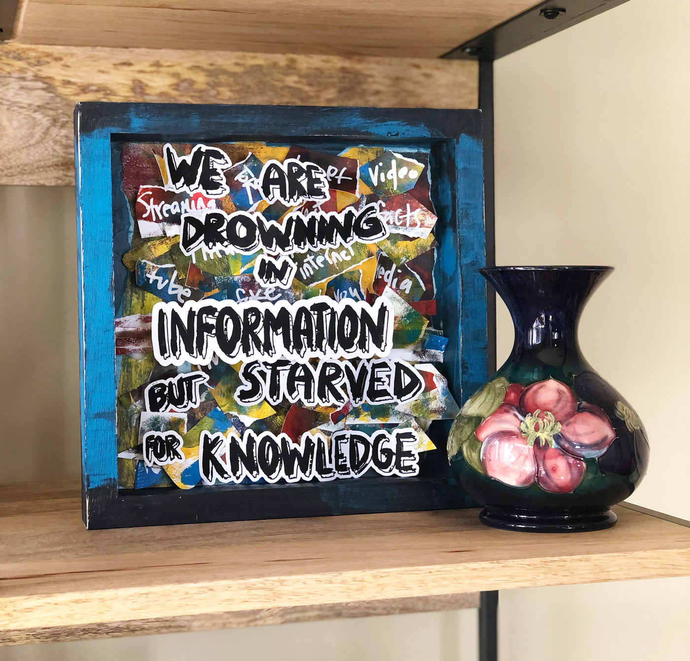 wooden box painted blue and black with brightly colored paper scraps and the words, "we are drowning in information but starved for knowledge."