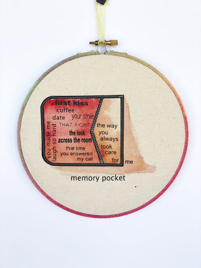 a round wooden painted hoop with canvas, a painted red pocket on its side with the words spilling out...memory pocket, first kiss, coffee date, your smile, the look across the room, that time you answered my call, you always made me laugh so har, the way you always took care for me.