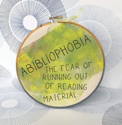 round wooden hoop with yellow-green paint and the words, "Abibliophobia - the fear of running out of reading material."