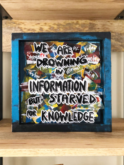 wooden box painted blue and black with brightly colored paper scraps and the words, "we are drowning in information but starved for knowledge."