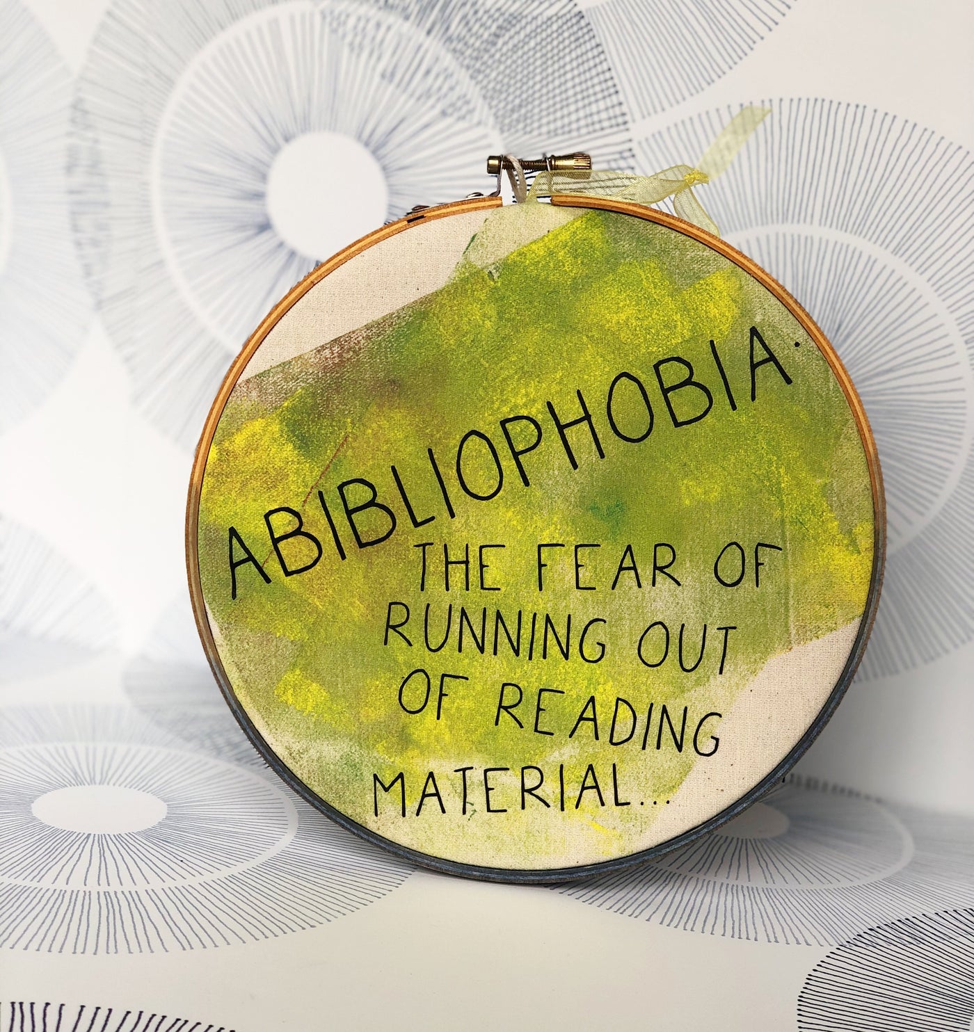 round wooden hoop with yellow-green paint and the words, "Abibliophobia - the fear of running out of reading material."