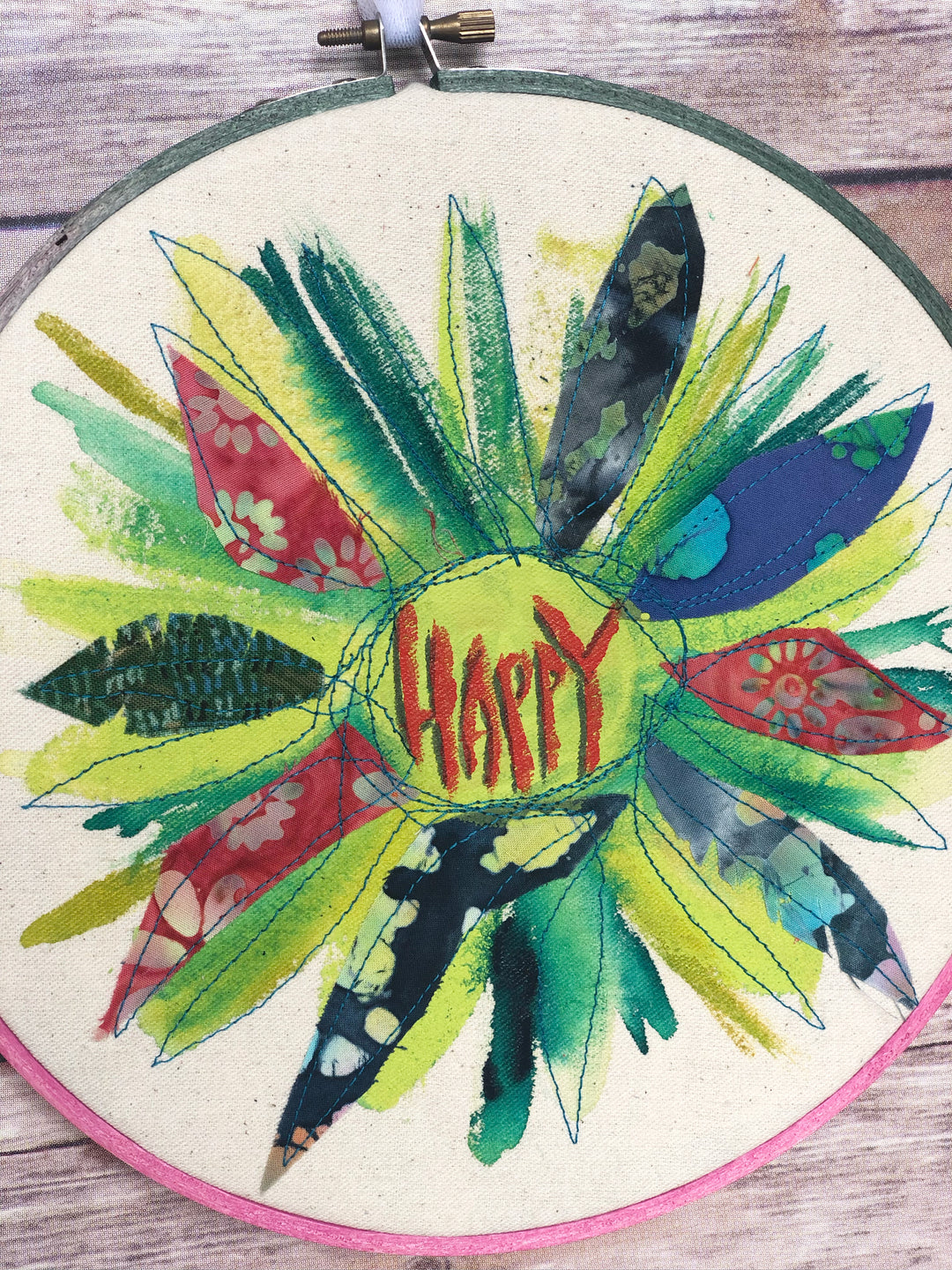 round dyed wooden hoop art, with painted and stitched fabric leaves in colors of yellow and orange and red, with the word 'happy' painted in the center