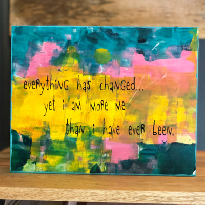 a painted wooden panel, with paint colors of teal, burnt yellow, red, coral and black, with the words, "everything has changed...yet I am more me than i have ever been."