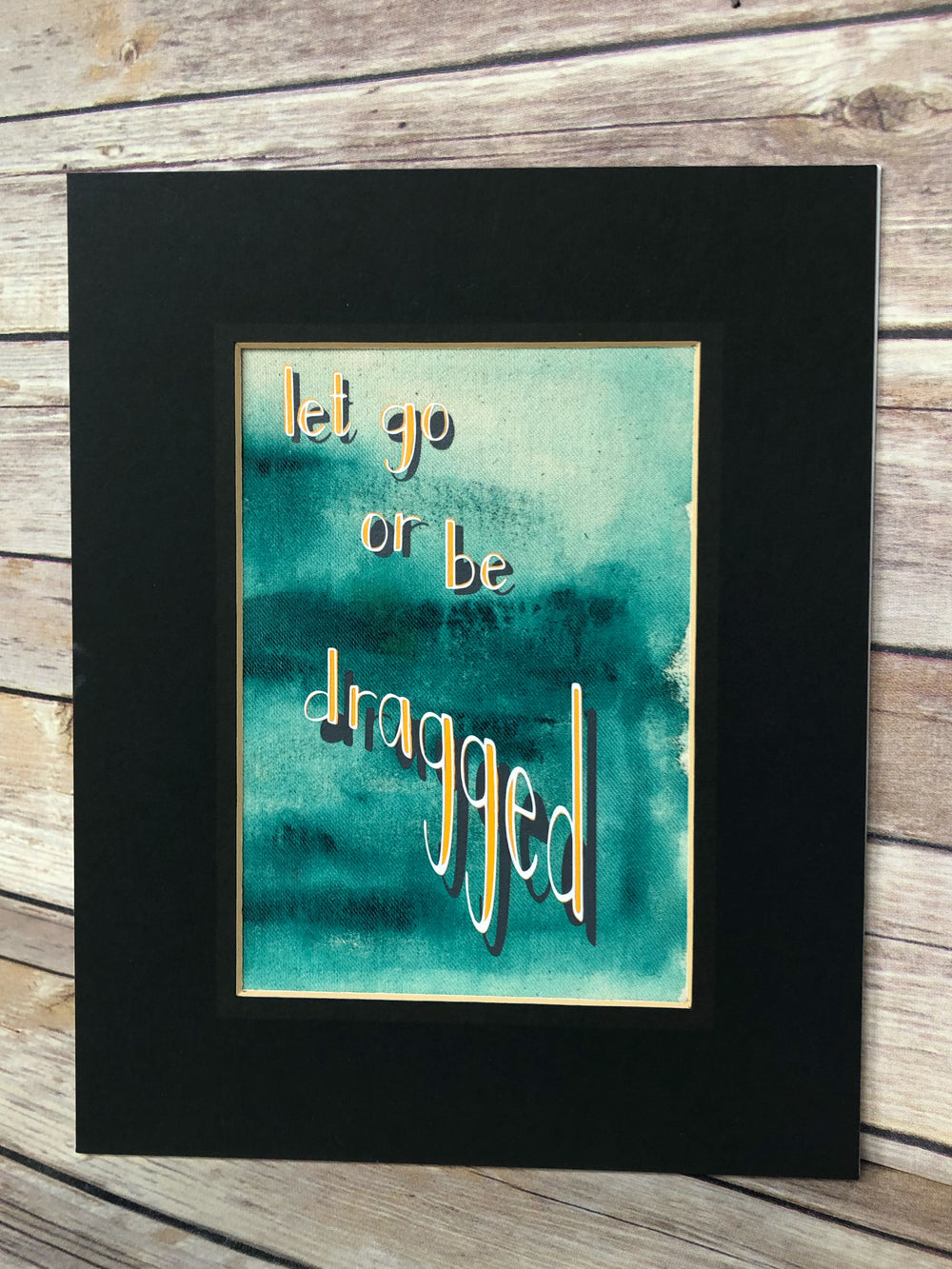 fabric print with green paint and the words, "let go or be dragged."