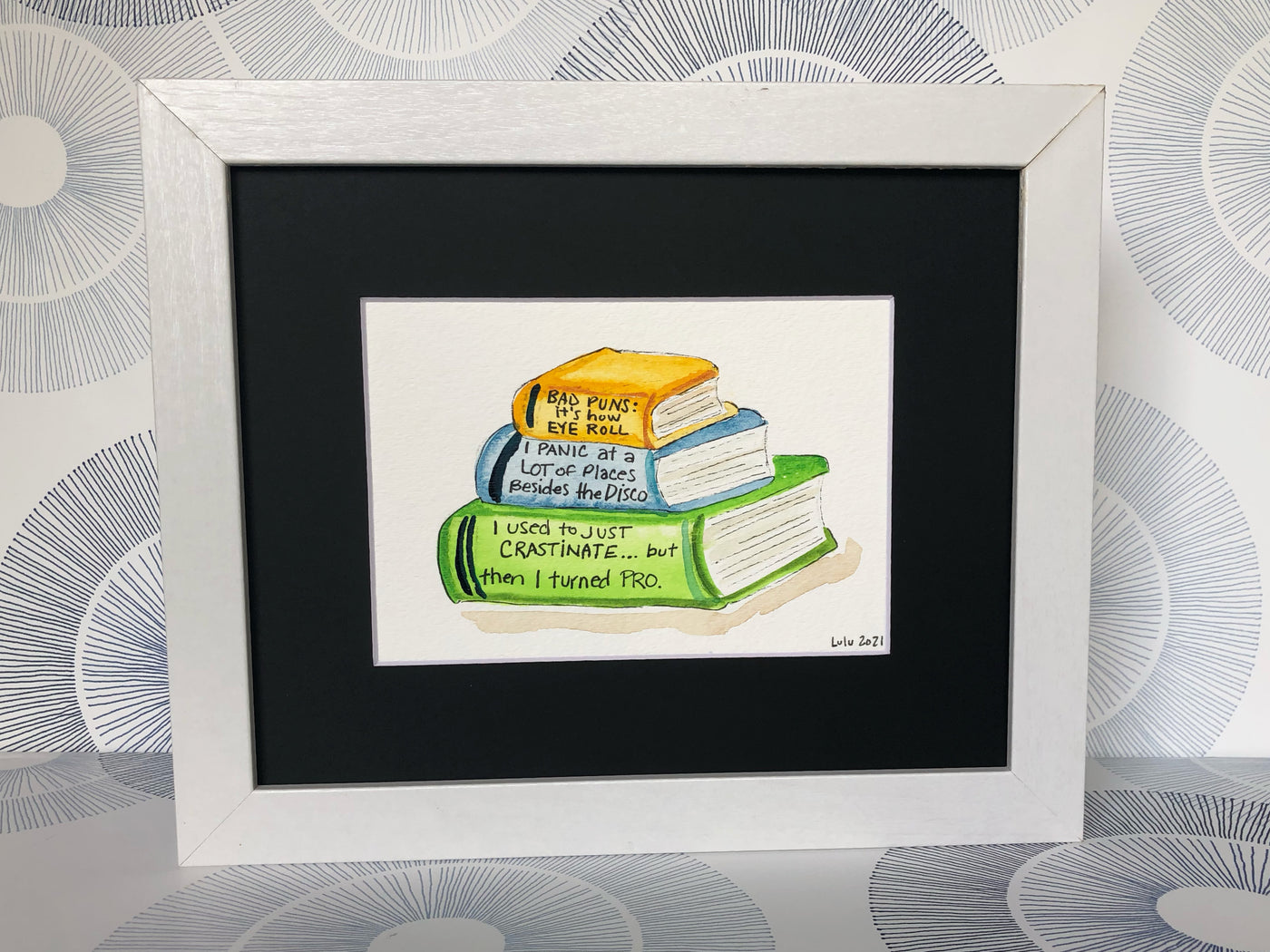 an original painted watercolor piece with three books in colors of burnt yellow, celery green and faded cerulean blue