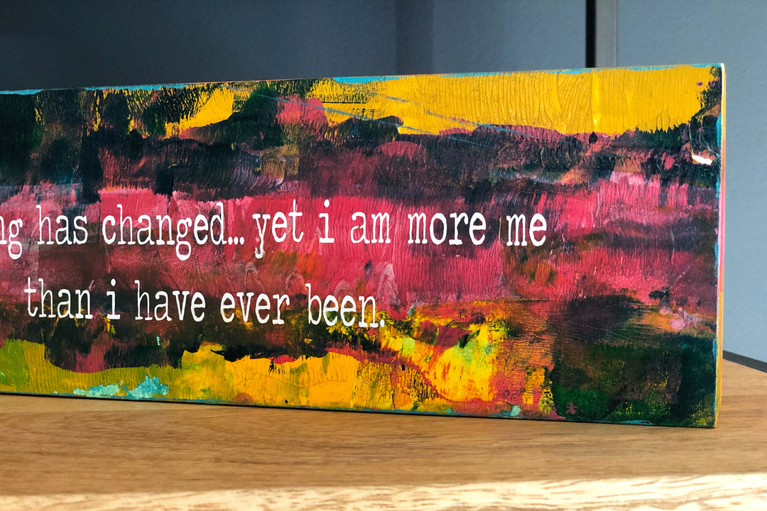 a painted wooden panel, with paint colors of teal, burnt yellow, red, coral and black, with the words, "everything has changed...yet I am more me than i have ever been."