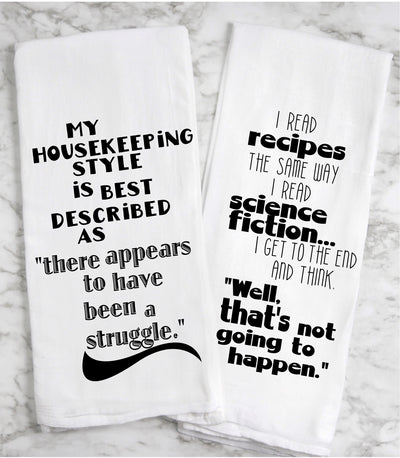 a white cotton kitchen towel with the words, "i read recipes the same way i read science fiction... i get to the end and think, "Well, ﻿that's﻿ not going to happen." A second white cotton kitchen towel with the words, "my housekeeping style is best described as 'there appears to have been a struggle.'