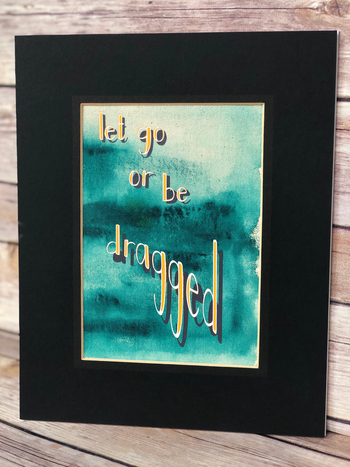 fabric print with green paint and the words, "let go or be dragged."