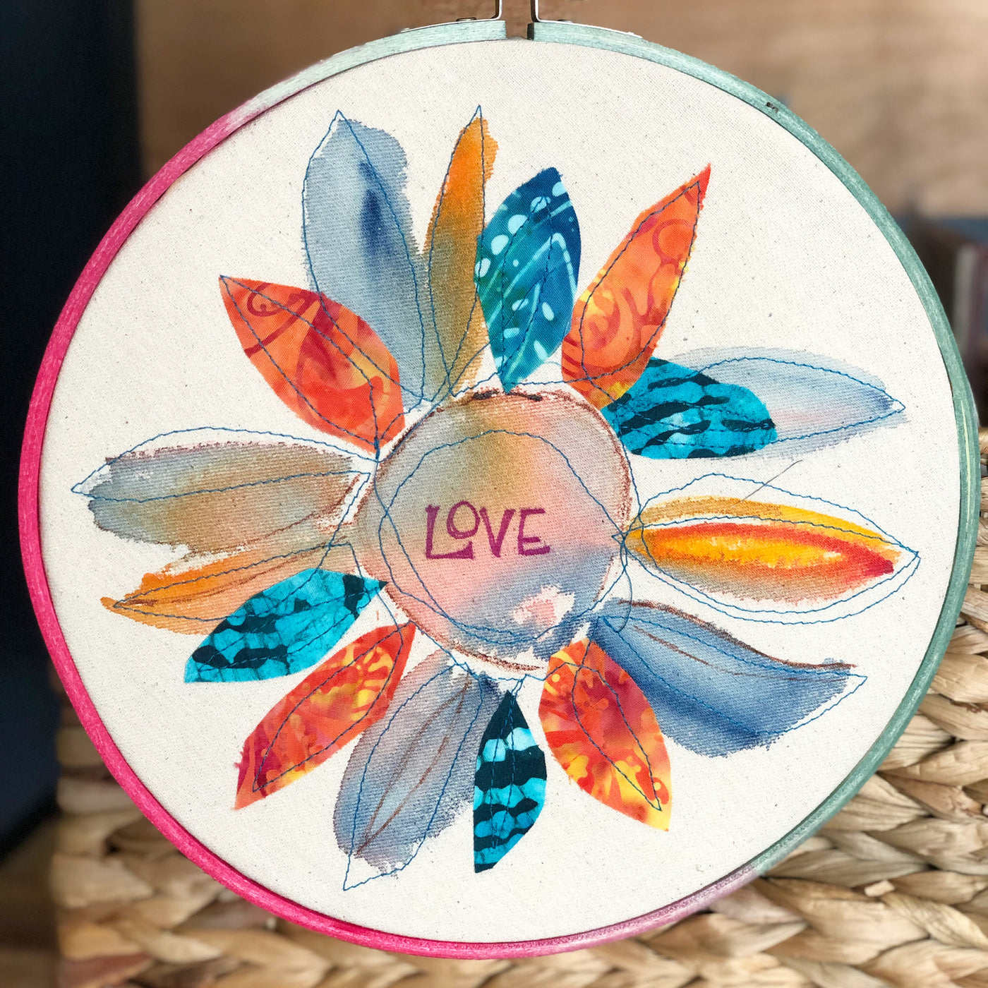 round dyed wooden hoop art, with painted and stitched fabric leaves in colors of blue and orange and yellow, with the word 'love' painted in the center