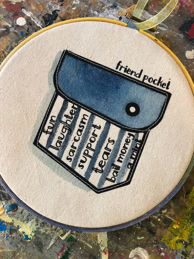 round painted wooden hoop with canvas and a painted blue pocket, containing the words 'friend pocket' and the words, fun, laughter, sarcasm, support, tears, bail money, a mint.'