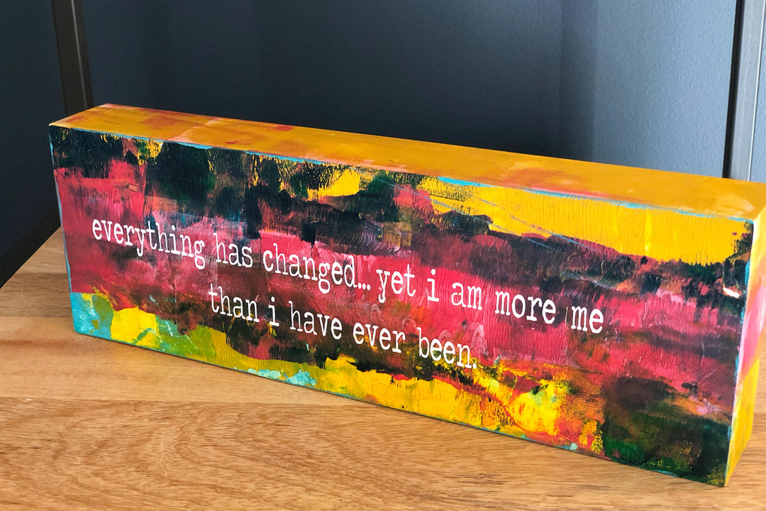 a painted wooden panel, with paint colors of teal, burnt yellow, red, coral and black, with the words, "everything has changed...yet I am more me than i have ever been."