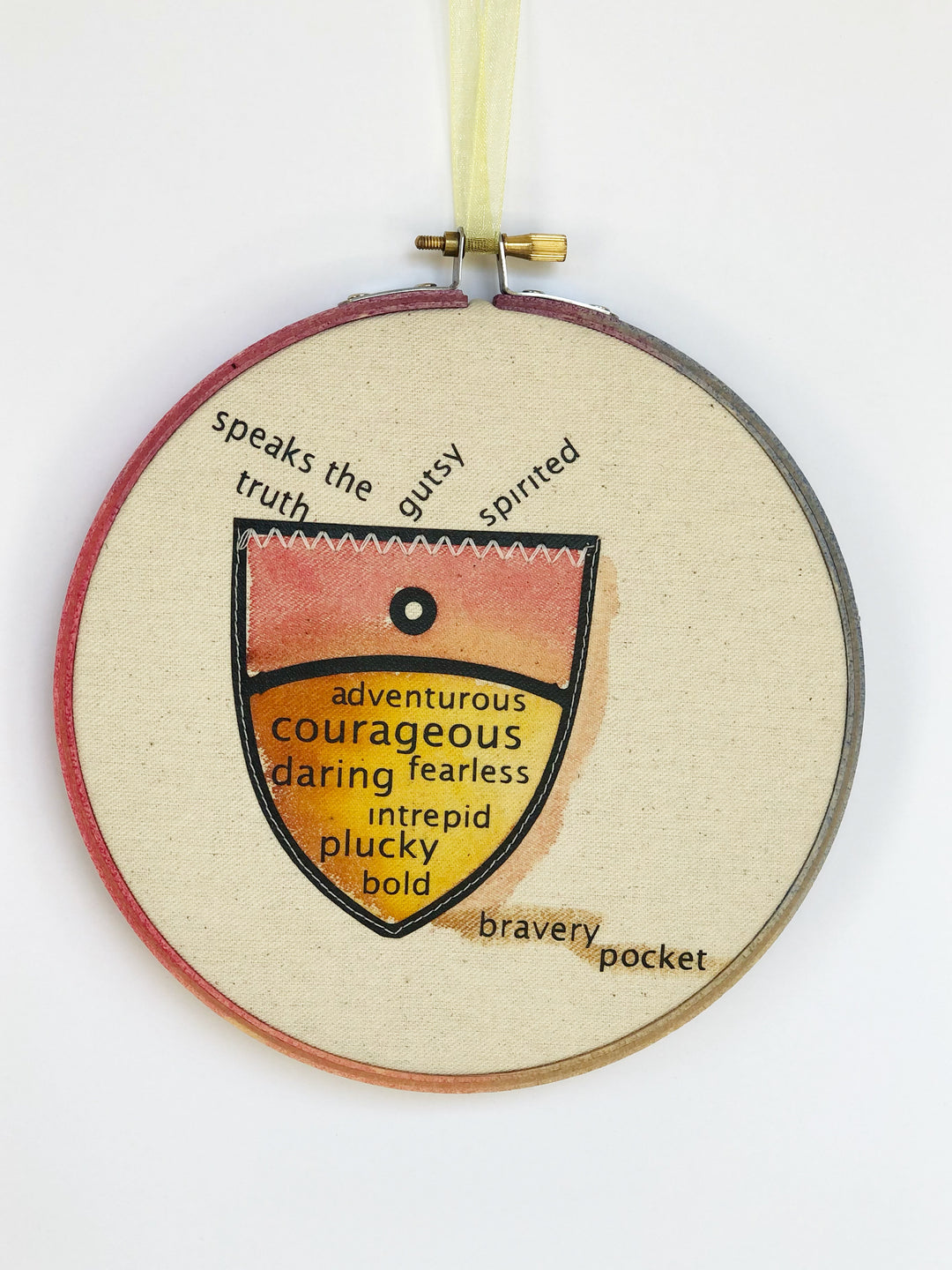 round painted wooden hoop with canvas and a painted pocket shape, filled with words about bravery, such as speaks the truth, gutsy, spirited, adventurous, courageous, fearless, daring, intrepid, plucky and bold