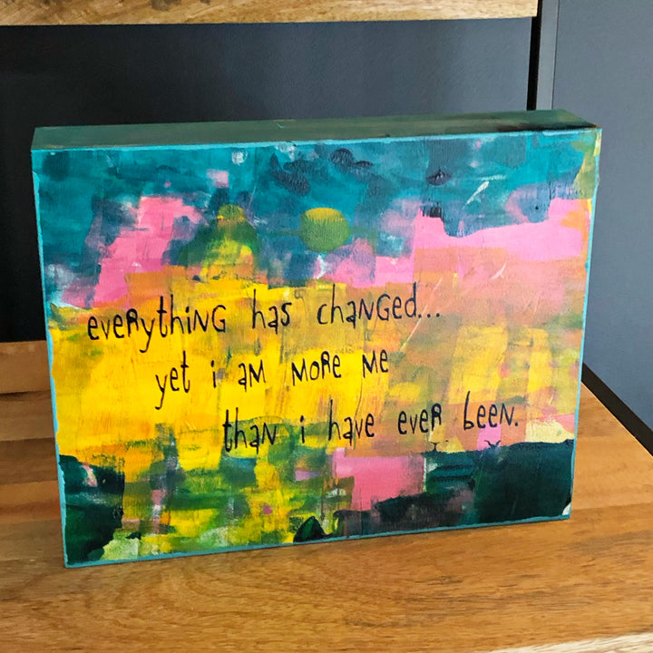 a painted wooden panel, with paint colors of teal, burnt yellow, red, coral and black, with the words, "everything has changed...yet I am more me than i have ever been."