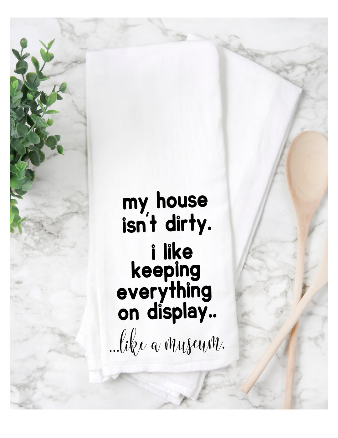 a white cotton kitchen towel with the words, "my house isn't dirty. I like keeping everything on display. like a museum."