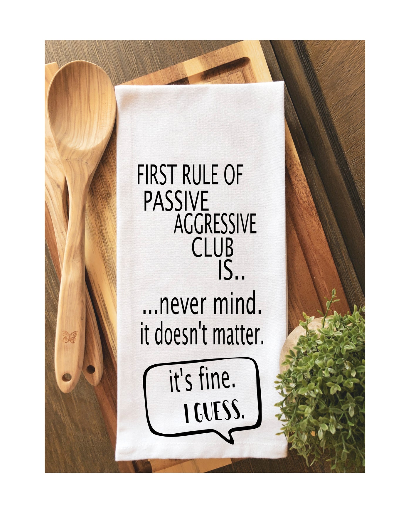 a white cotton kitchen towel with the words, "first rule of passive aggressive club is..never mind. it doesn't matter. it's fine. I guess."